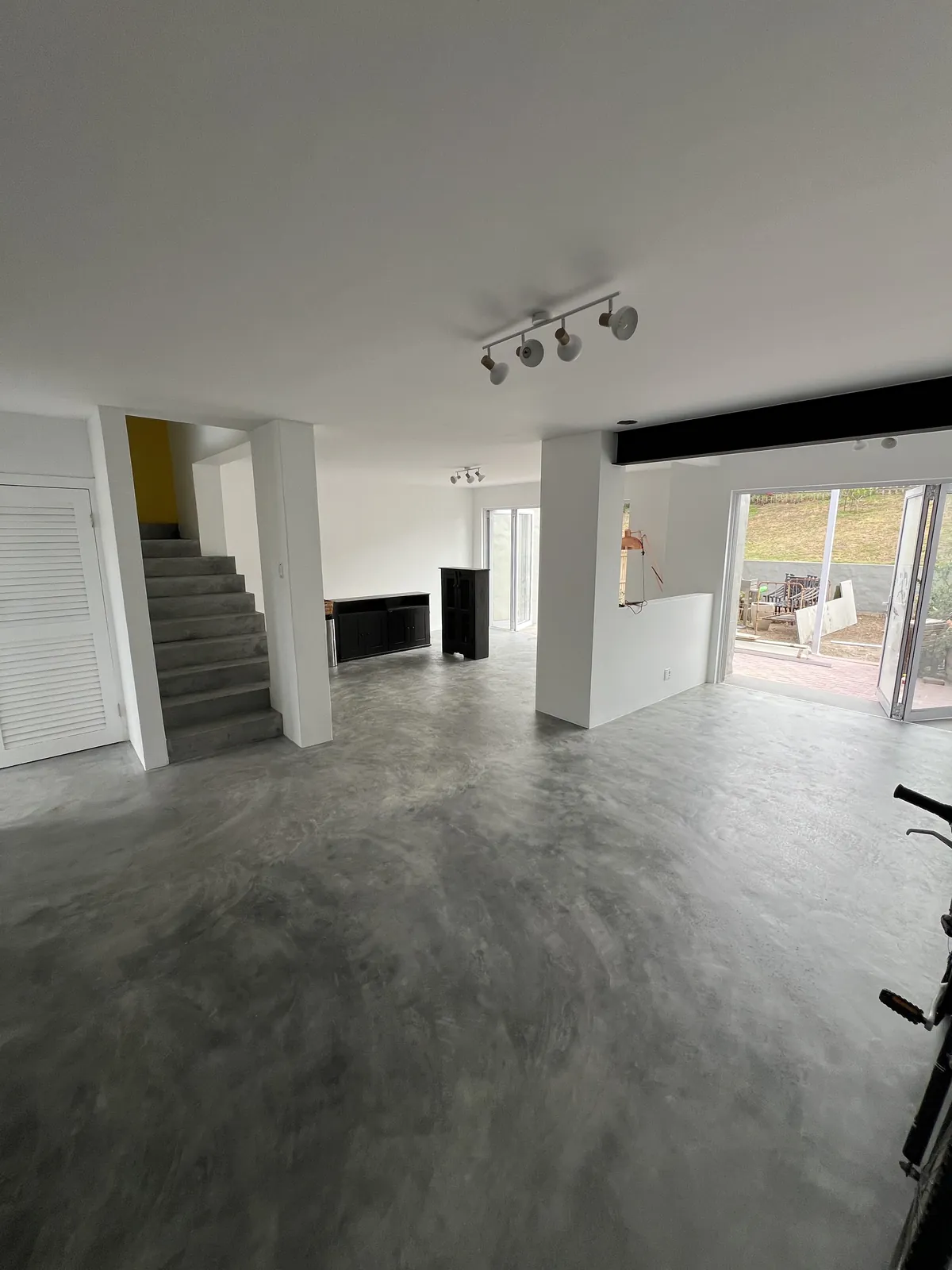 Finished open-plan ground floor with microcement floors, concrete stairs and folding doors to the garden