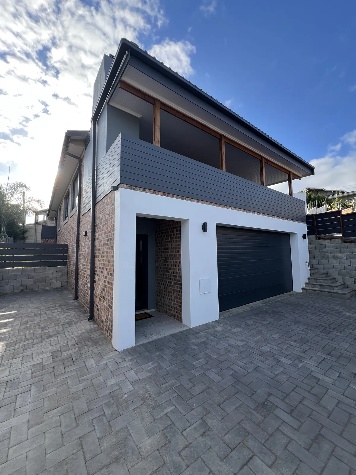 House Elwena finished: white garage frame, dark grooved plaster, timber pergola and paving