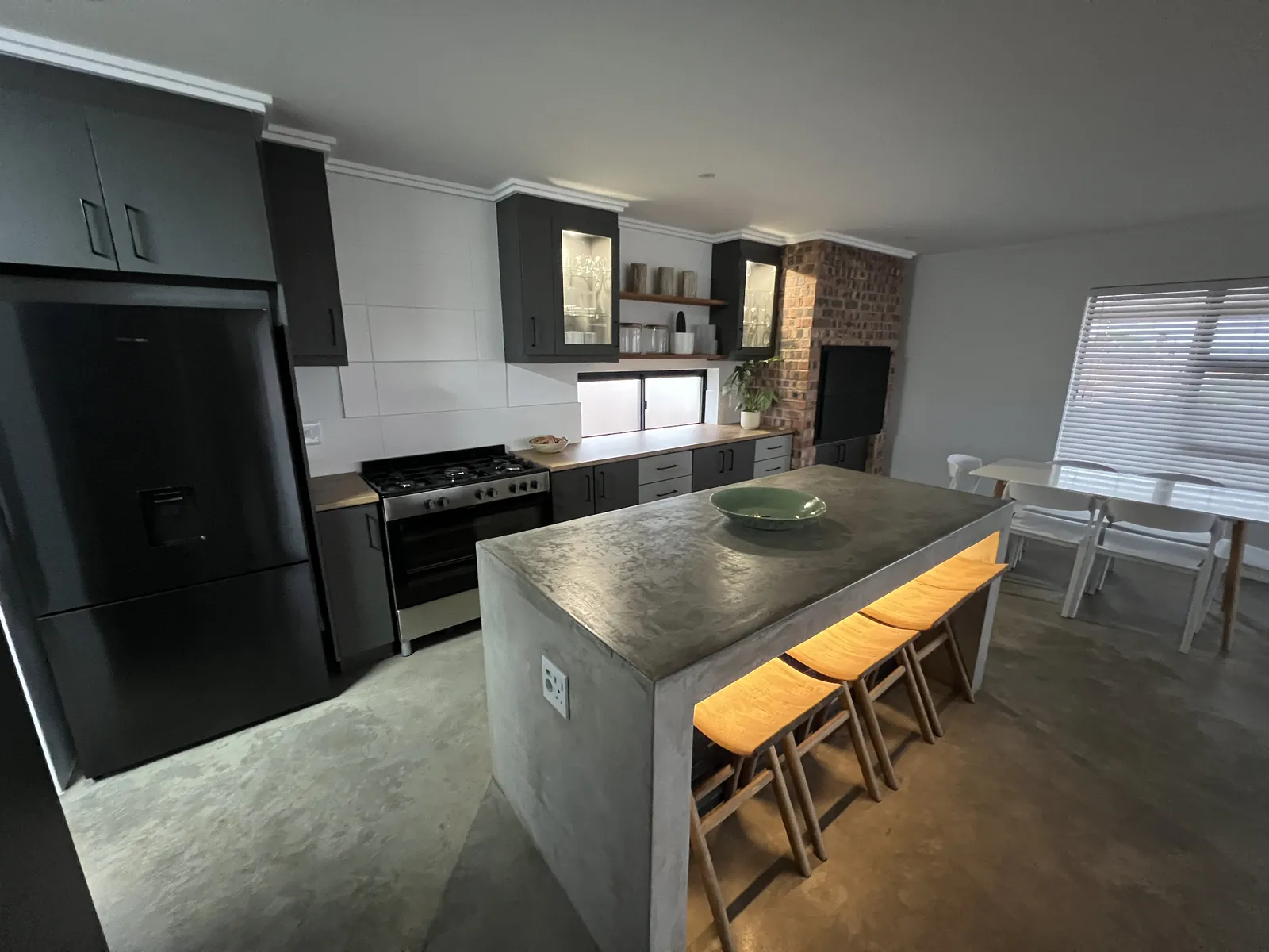 Finished kitchen with a concrete island, face-brick braai and dark cabinets
